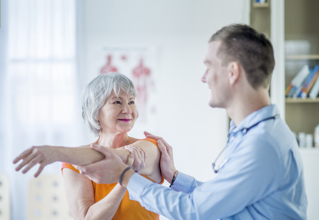 Rechts im Bild ist ein Arzt. Links im Bild eine Patientin. Der Arzt untersucht den Arm der Patientin. 