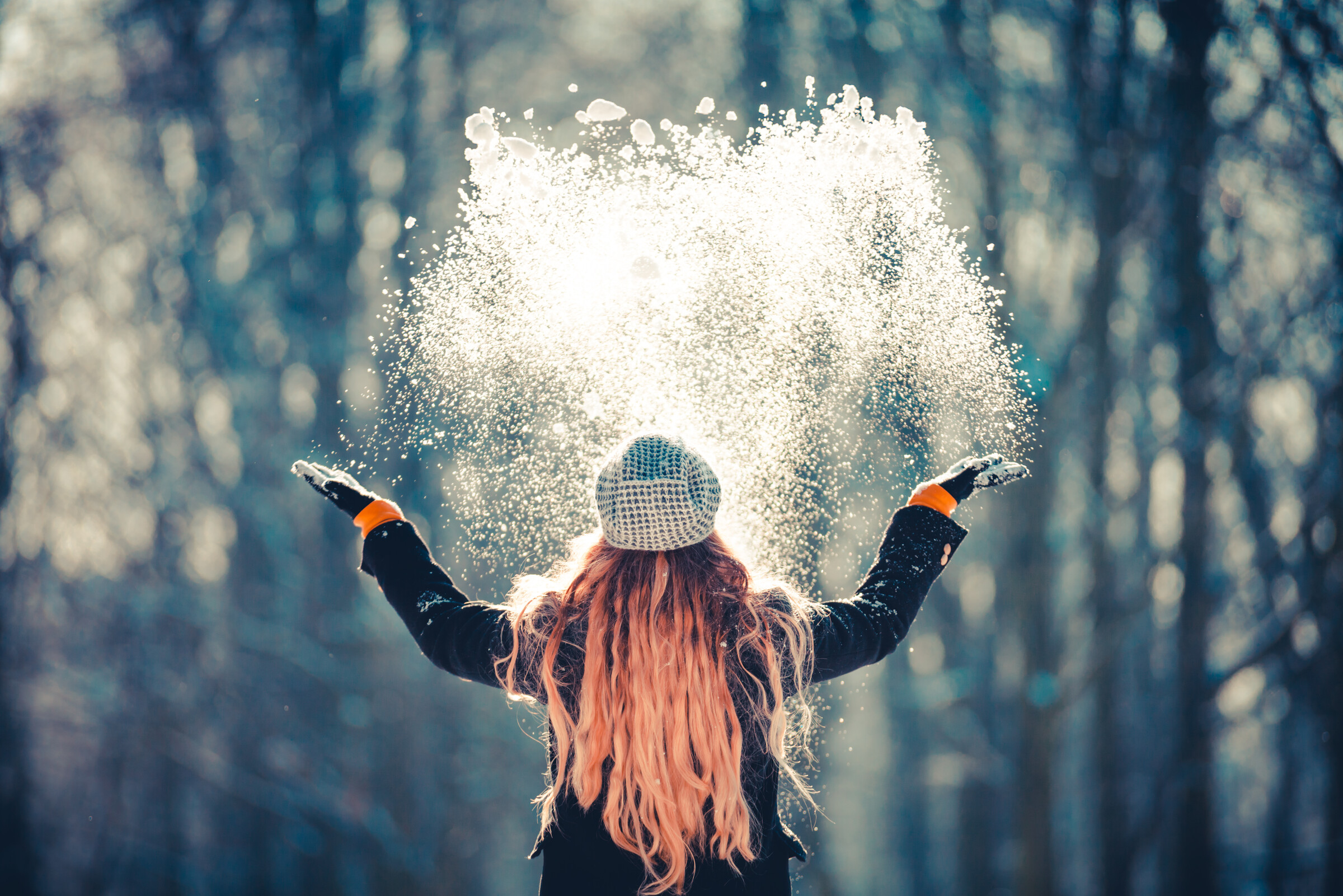 Junges Mädchen wirft an einem sonnigen Wintertag Schnee in die Luft, Rückansicht
