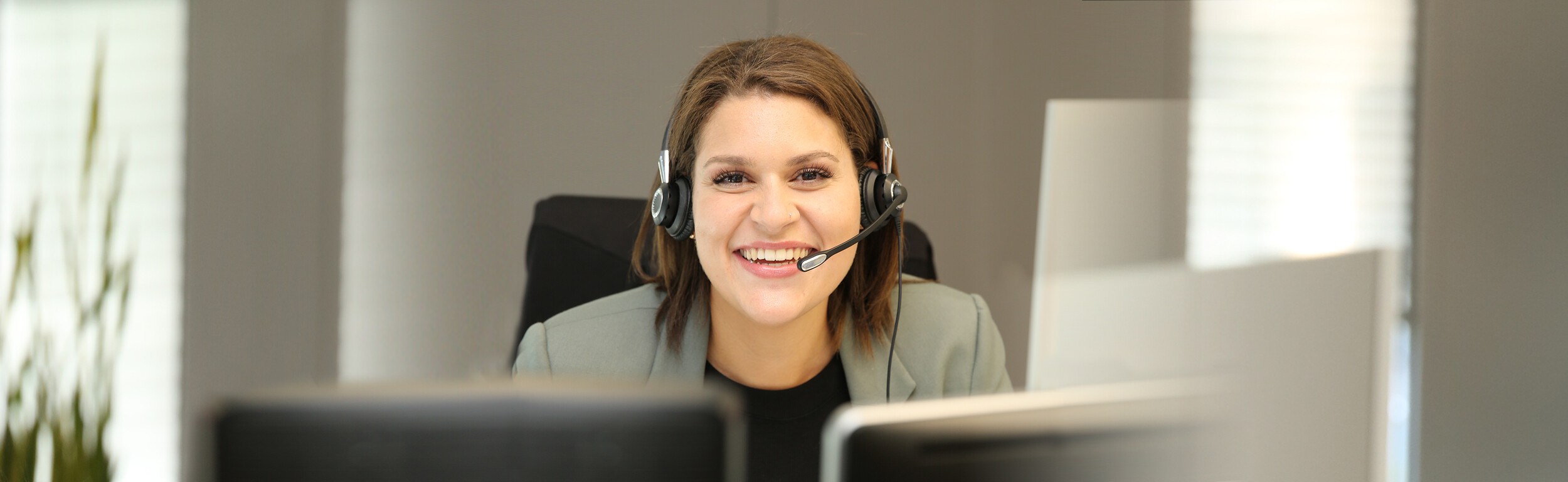 Frau mit einem Headset sitzt lächelnd vor einem Computer.