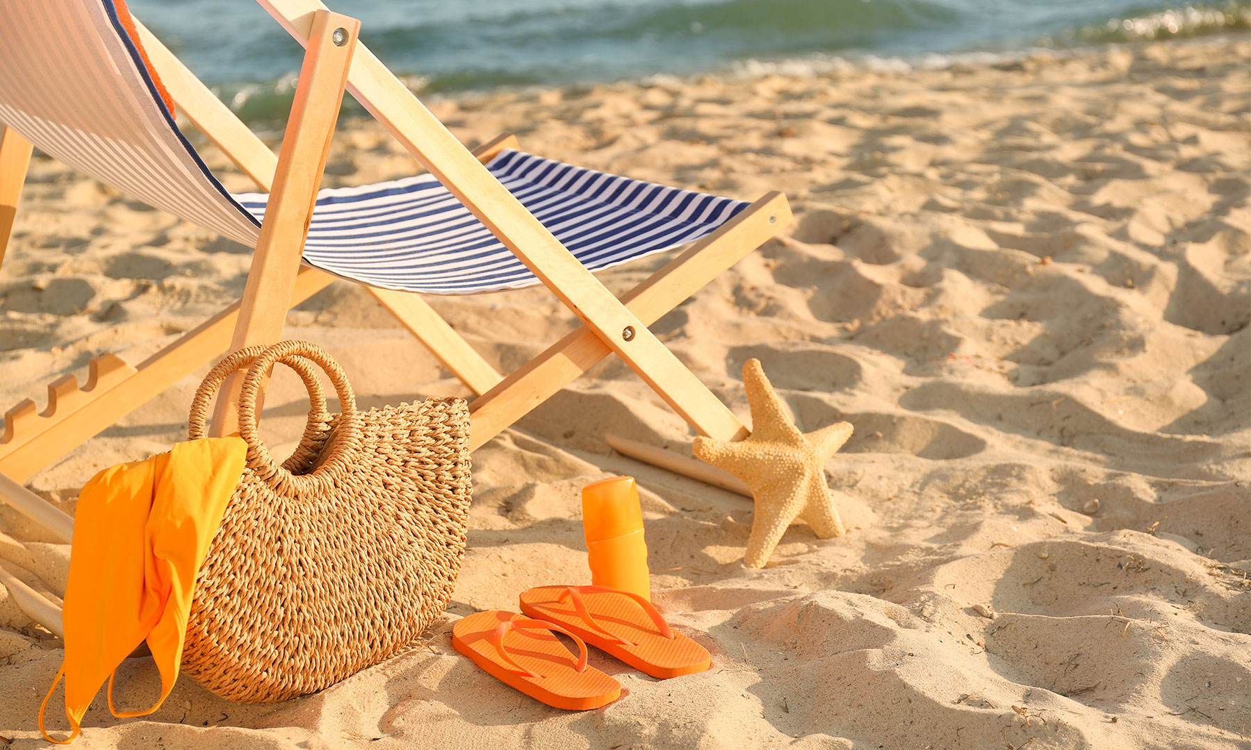 Liegestuhl mit Strandtasche und Flipflops im Sand