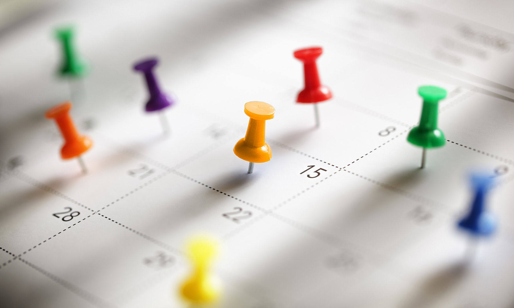 Auf einem Kalender befinden sich bunte Pinnadeln. 